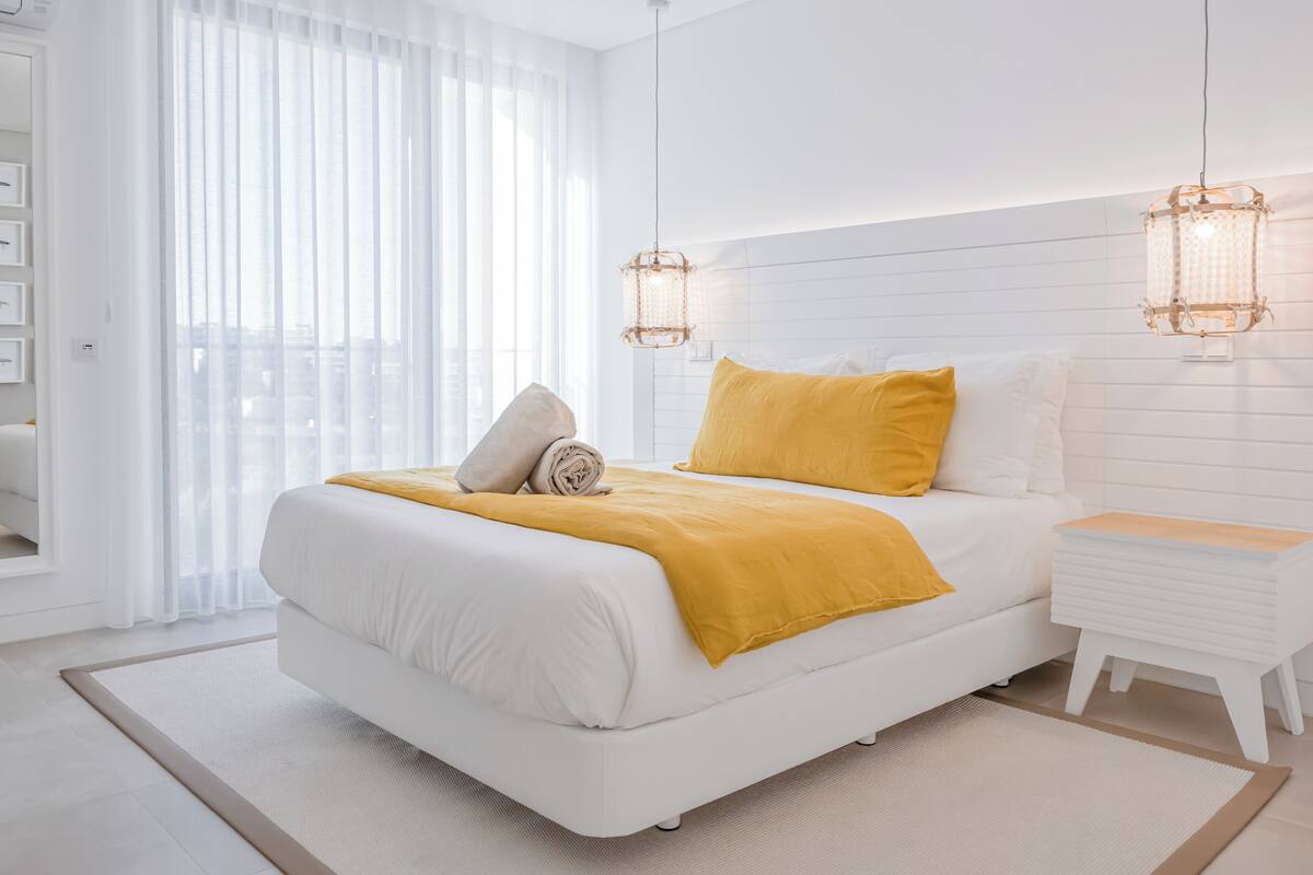 Ein modernes Schlafzimmer mit einem großen Bett, weißen Wänden und einem Fenster mit durchscheinenden Vorhängen.
