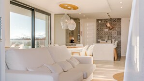 Un salon moderne avec un canapé blanc, un coin repas avec une table et des chaises, et une cuisine en arrière-plan.