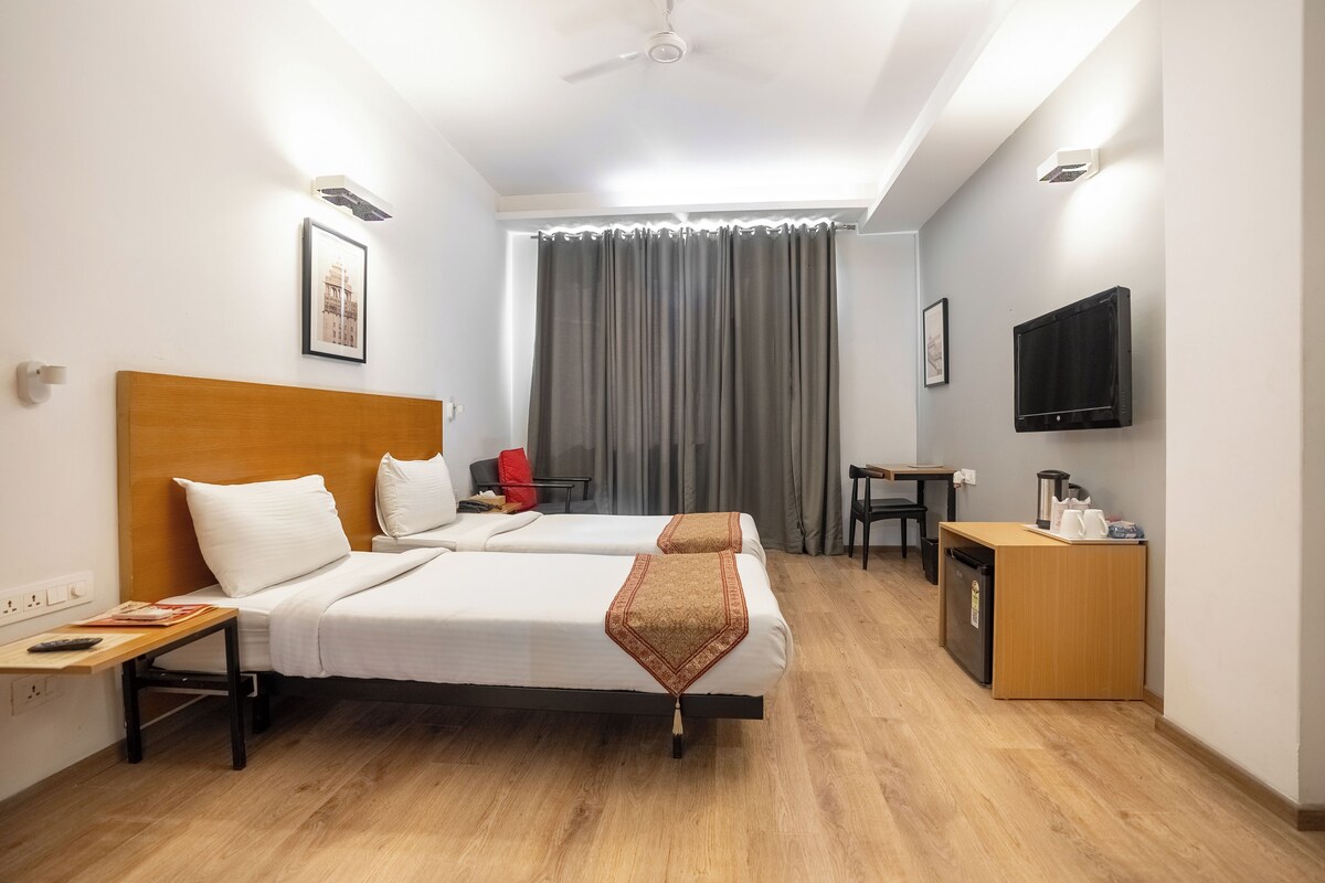 A hotel room with two beds, a desk, a TV, and a small kitchenette.