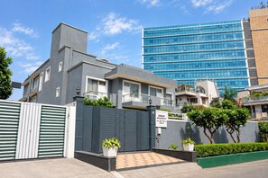 Un moderno edificio residencial con entrada vigilada, un cartel que indica que forma parte de Enkay Residency, y un edificio de vidrio azul al fondo.