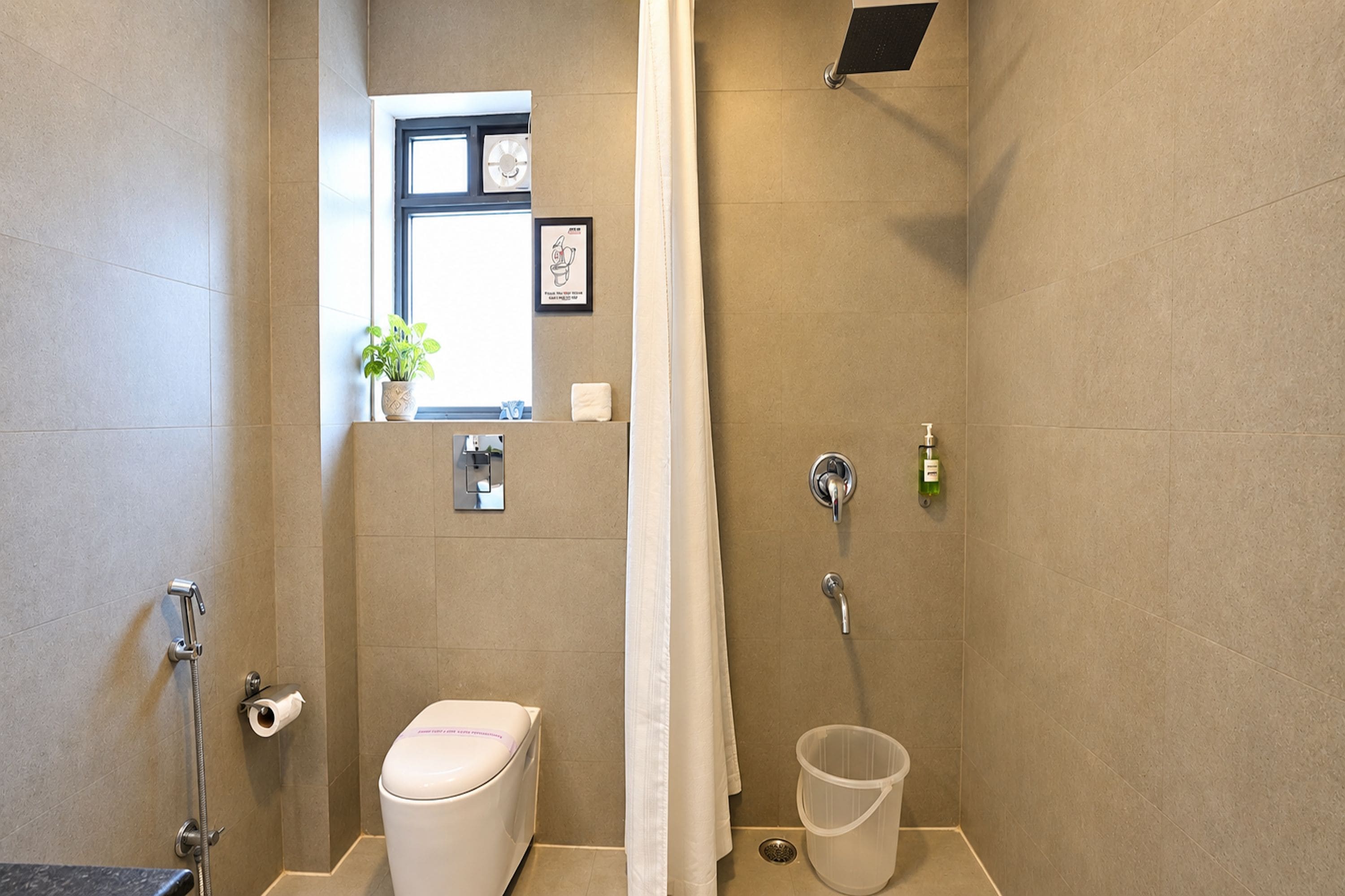 Un baño con inodoro, ducha y una pequeña ventana con una planta.