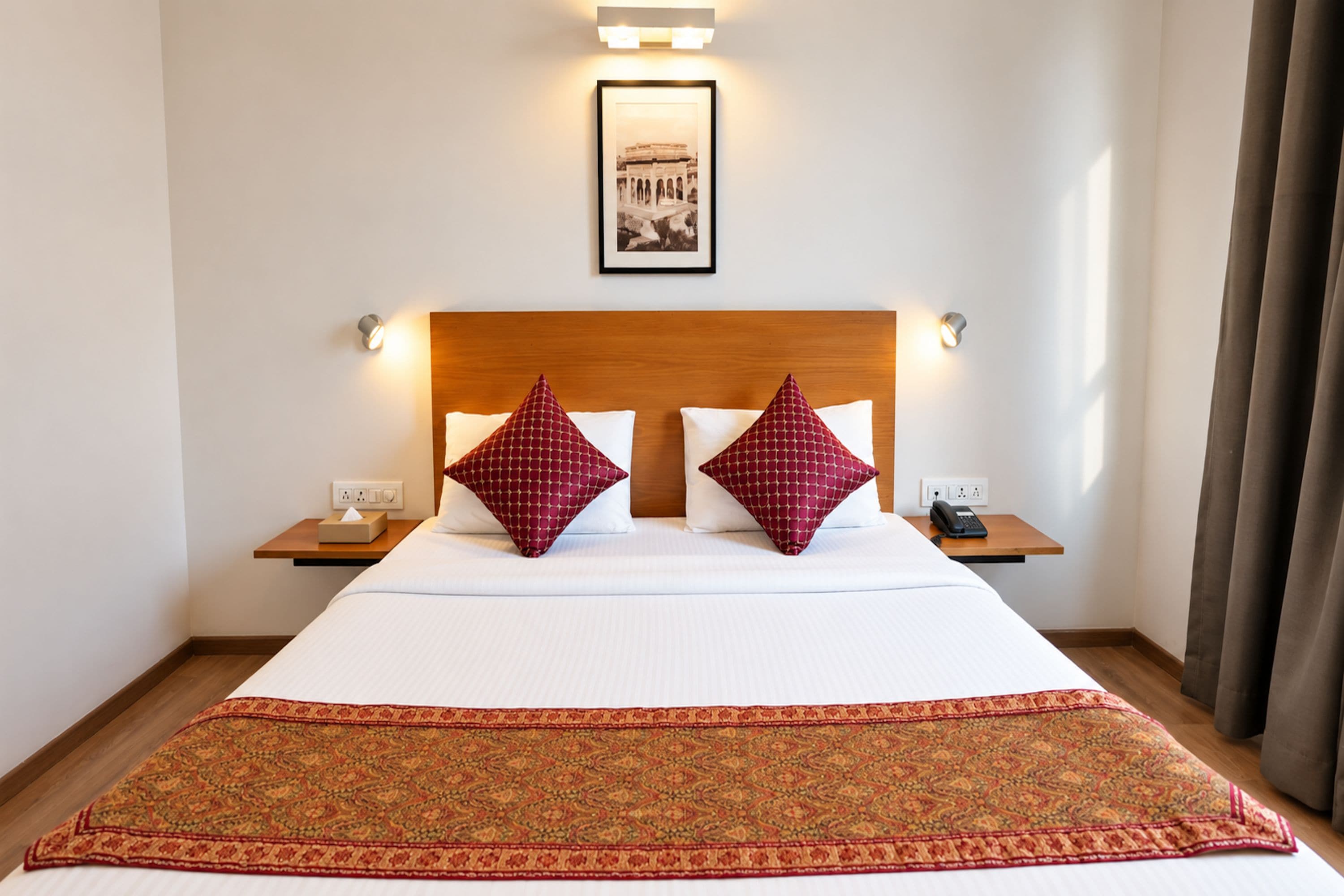 A hotel room with a large bed, two bedside tables, a telephone, and a framed picture on the wall.