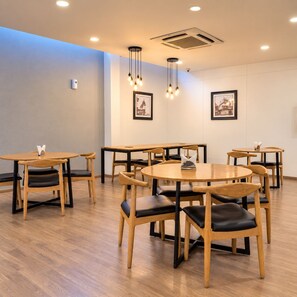 Un espace repas avec des tables et des chaises rondes, un éclairage encastré au plafond et des tableaux encadrés accrochés aux murs.