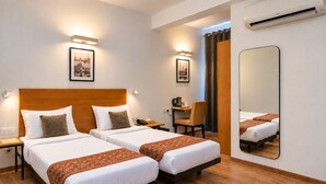A hotel room with two beds, a desk, a chair, a mirror, and an air conditioning unit. - Enkay Residency Sector 15 (Gurugram)