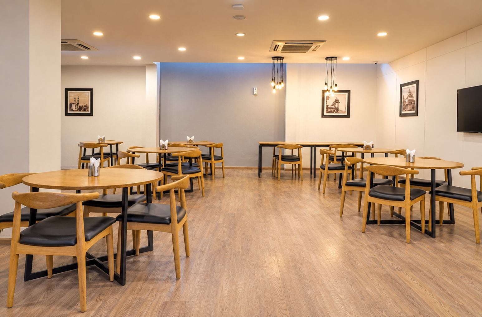 A conference room with multiple tables and chairs, air conditioning vents, and framed pictures on the walls.