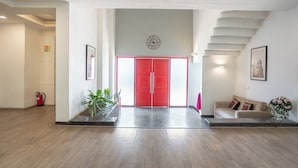 A spacious lobby with a red door, a staircase, and a sofa with cushions. - Enkay Residency Sector 15 (Gurugram)