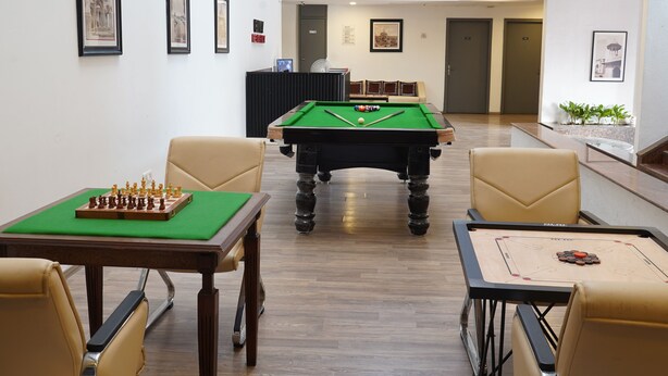 A pool table with a green felt top, surrounded by beige chairs, in a room with framed pictures on the walls. - Enkay Residency Sector 15 (Gurugram)