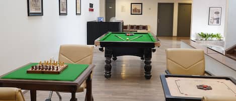 A pool table with a green felt top, surrounded by beige chairs, in a room with framed pictures on the walls.