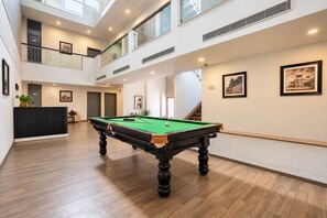 A pool table in a spacious indoor area with a high ceiling, wooden flooring, and a staircase leading to an upper level. - Enkay Residency Sector 15 (Gurugram)