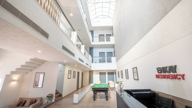 A spacious atrium with a pool table, a staircase, and a sign for EnKay Residency. - Enkay Residency Sector 15 (Gurugram)