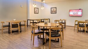 A dining area with round tables and chairs, a television screen, and framed pictures on the wall. - Enkay Residency Sector 15 (Gurugram)
