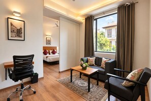 Une chambre d’hôtel moderne, équipée d’un lit, d’un canapé, d’un bureau et d’une chaise. On y trouve une fenêtre avec des rideaux, un luminaire fixé au mur et un tableau encadré.