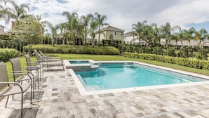 Piscina retangular com um deck ladrilhado, rodeada por cadeiras e palmeiras.