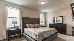 Quarto com uma cama grande, duas mesas de cabeceira, cômoda e janela com cortinas.