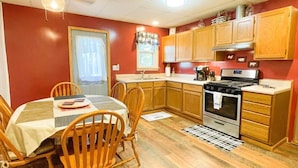 A compact kitchen with wooden cabinets, a stove, and a dining table with chairs. - Cozy private Lakehouse with prime fishing, hunting, and lake access. (Webber)