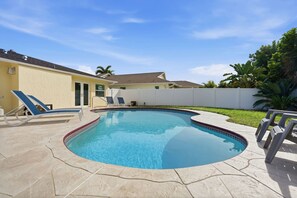Ein Pool mit geschwungener Kante, umgeben von einem weißen Zaun, und ein gelbes Gebäude im Hintergrund.
