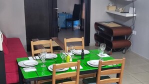A dining area with a green table set for two, wooden chairs, and a red couch in the background. - 2br-7 Guests-free Parking-pool-aircon (Paralimni)