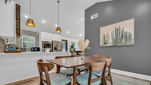 A modern kitchen with white cabinets, a stainless steel refrigerator, and a dining area with a wooden table and chairs.