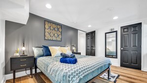 A modern bedroom with a bed, nightstands, a dresser, and a large mirror.