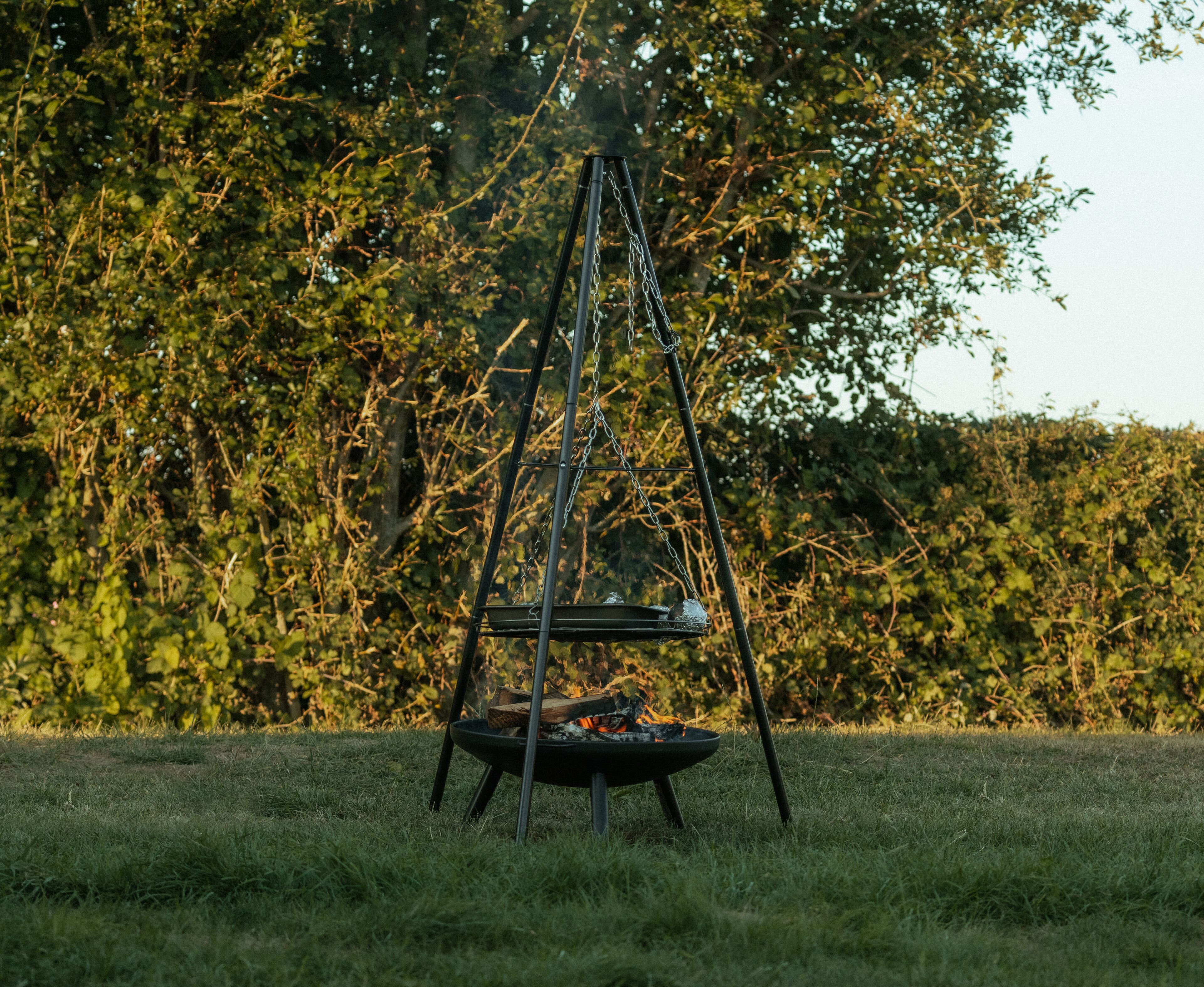 A metal swing set with a fire pit in the middle, surrounded by grass and trees.