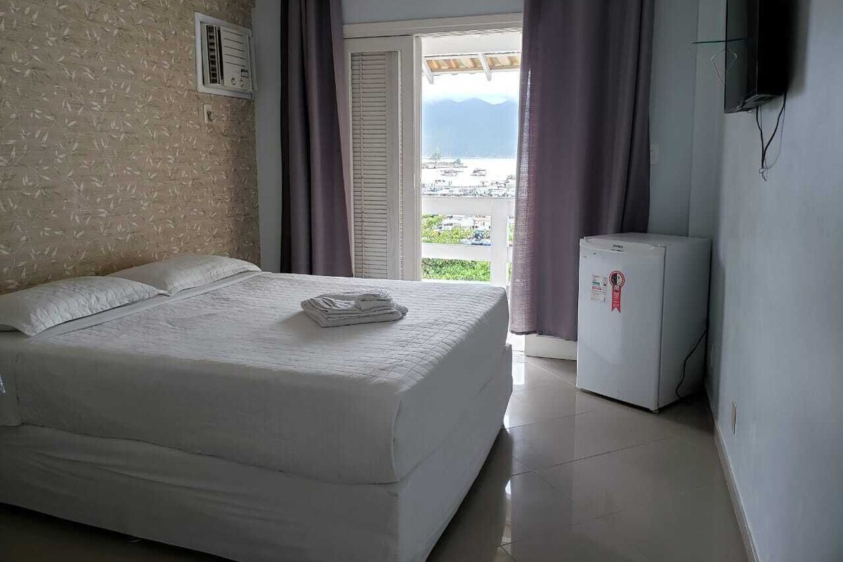 Un dormitorio con una cama, un refrigerador pequeño, un televisor y una ventana con cortinas.