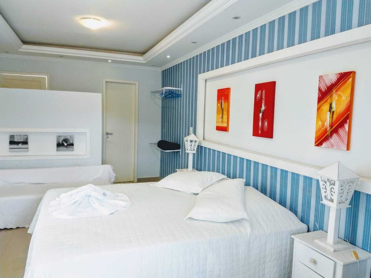 Una habitación de hotel con una cama grande, dos mesitas de noche, un armario y tres cuadros en la pared.