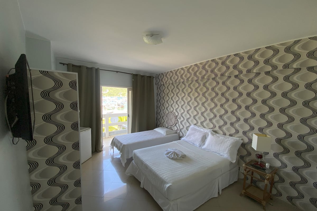 Ein Hotelzimmer mit zwei Betten, einem kleinen Tisch mit einer Lampe und Blick auf den Pool durch die Tür.