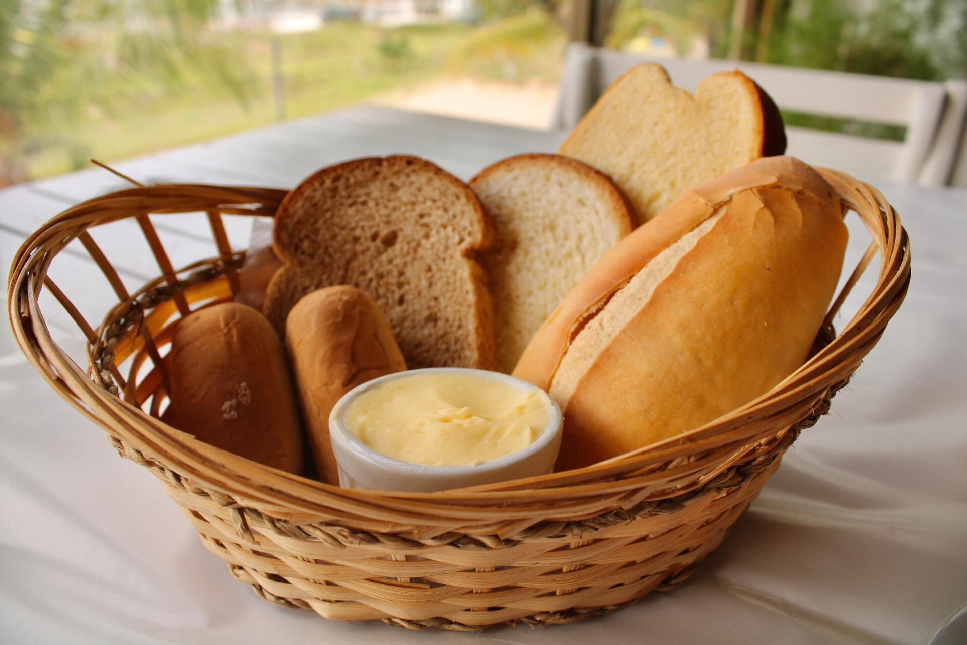 A wicker basket containing various types of bread and a small bowl of butter on a table.