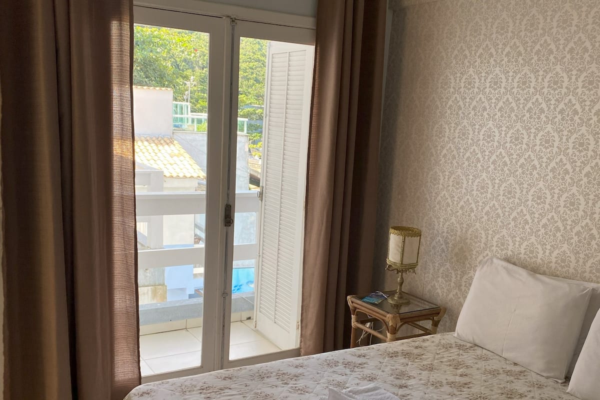Ein Hotelzimmer mit Bett, Nachttisch, Lampe und Blick auf einen Pool durch eine Schiebetür.