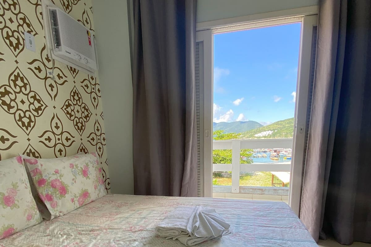 Ein Schlafzimmer mit einem Bett, floralem Bettbezug, einem Fenster mit Vorhängen und Blick auf einen Pool und Berge.