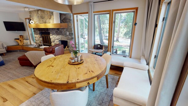Ein geräumiges Wohnzimmer mit Kamin aus Stein, einem runden Esstisch aus Holz und einer gemütlichen Sitzecke mit weißem Sofa und Sesseln.