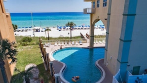 A pool area with a view of the beach, lounge chairs, and umbrellas.