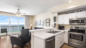 A modern kitchen with white cabinets, stainless steel appliances, and a view of the ocean through large windows.