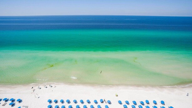 A beach with clear turquoise water, white sand, and blue umbrellas.