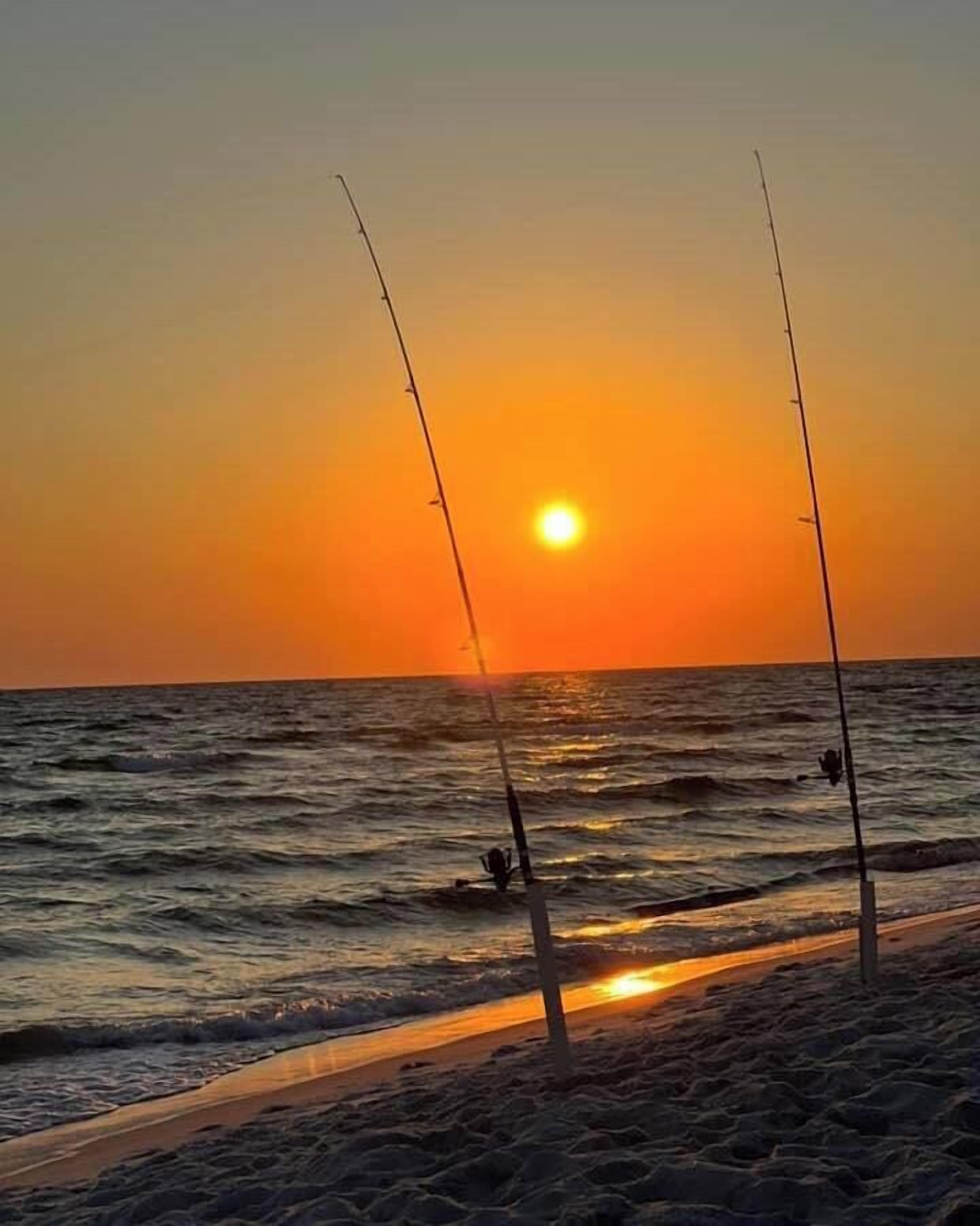 A beach scene with two fishing rods and the sun setting over the ocean.