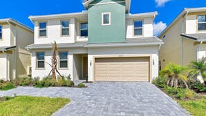 Un immeuble résidentiel de deux étages avec une porte de garage beige, un mur d’accent vert et une allée pavée.