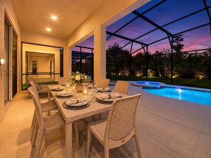 An outdoor dining area with a pool, wicker furniture, and a view of the surrounding landscape. - 12Bd Vacation Mansion For 30 Guests. Prime Disney Location, Amazing Value! (Kissimmee)