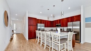 Une cuisine moderne avec des meubles rouges, des appareils en acier inoxydable et un îlot central doté de chaises blanches.