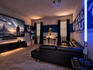 A room with a large flat-screen TV, a leather sofa, a small table, and Star Wars-themed decor. - 12Bd Vacation Mansion For 30 Guests. Prime Disney Location, Amazing Value! (Kissimmee)