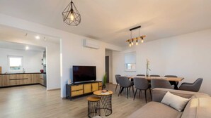 Ein modernes Wohnzimmer mit Sofa, Fernseher, Esstisch und Stühlen.