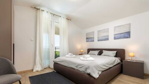 Ein Schlafzimmer mit einem großen Bett, einem Nachttisch, einem Stuhl und Blick ins Freie durch ein Fenster.