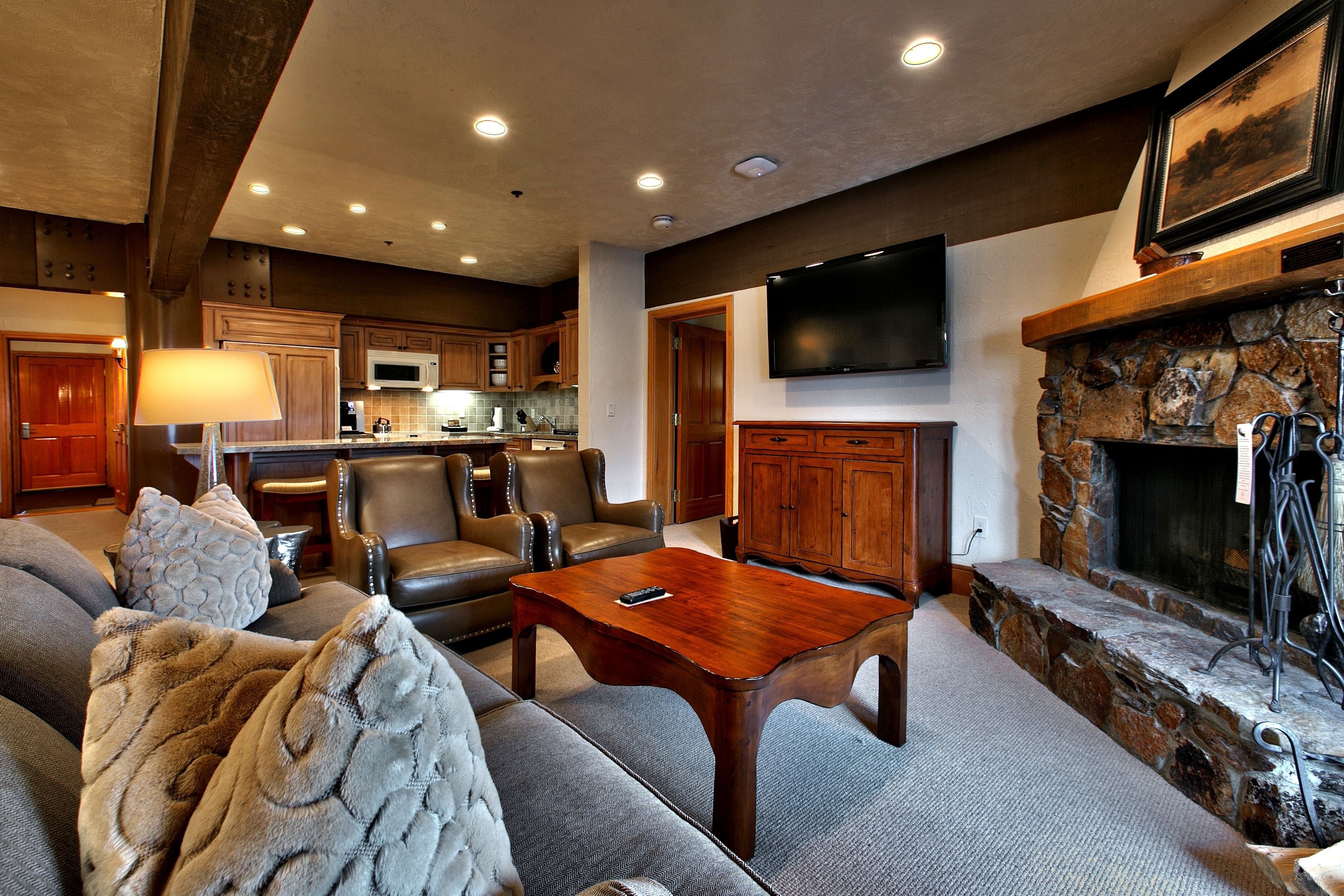 A spacious living room with a fireplace, leather sofas, and a flat-screen TV mounted above it.