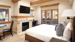 Un dormitorio con chimenea, cama, televisor y balcón con mobiliario exterior.