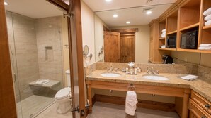 A modern bathroom with a glass shower enclosure, double sinks, wooden cabinetry, and a built-in microwave.