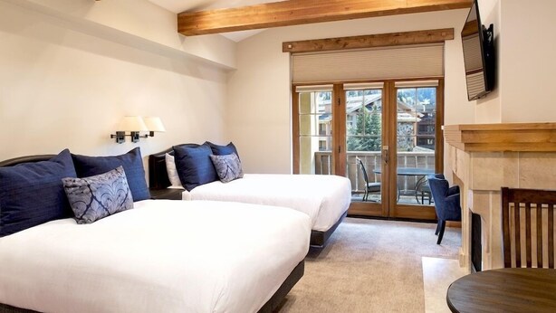 A bedroom with two beds, a fireplace, and a sliding glass door to a balcony.