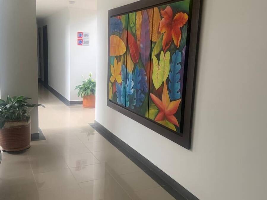 Een gang met een groot bloemenkunstwerk aan de muur, potplanten en een bordje met de tekst 'niet roken'.