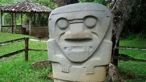 A stone monument with a carved face, surrounded by a wooden fence and a gazebo in the background. - Hotel Andinos Plaza (Pitalito)