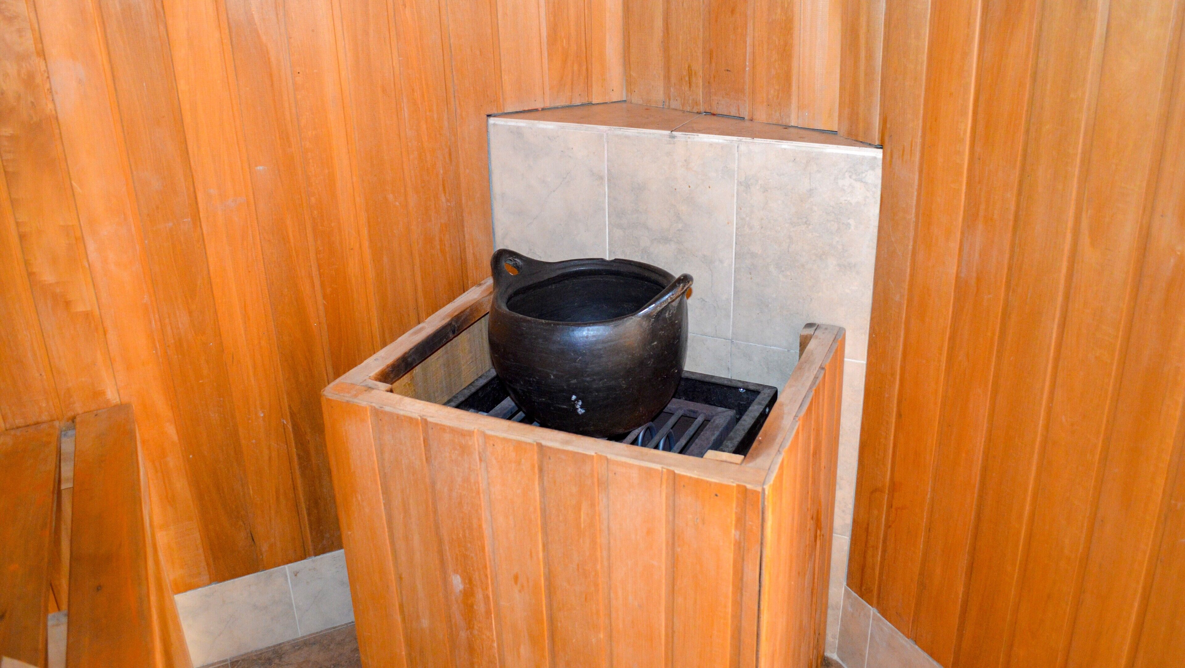 Un sauna en bois avec un récipient en céramique noire placé au centre.