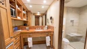 Un baño con tocador de madera, lavamanos, espejo y ducha con cerramiento de vidrio.