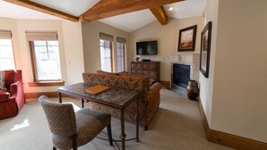 A living room with a wooden ceiling, a fireplace, a television, and a patterned sofa. - Deluxe King 1 Bedroom Hotel Room by RedAwning (Park City)